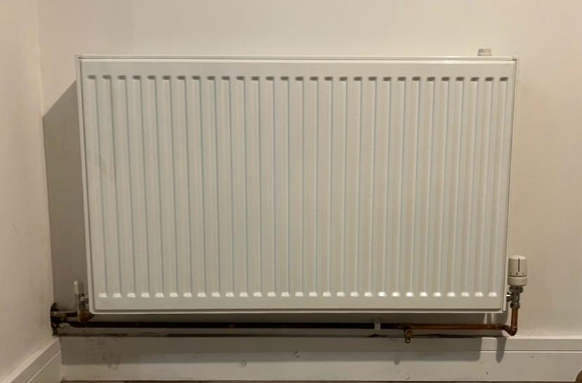 Newly installed white panel radiator with copper pipework below
